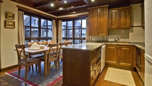 A kitchen with wooden cabinets, a granite countertop, and a dining area with a table and chairs. - Abetos - Val de Ruda (Baqueira)