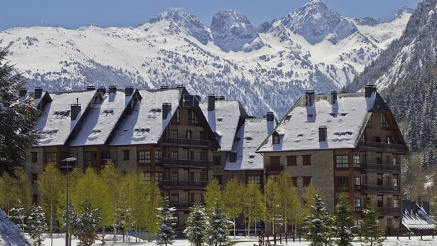 A row of chalet-style buildings with multiple balconies, set against a backdrop of snow-covered mountains. - Abetos - Val de Ruda (Baqueira)