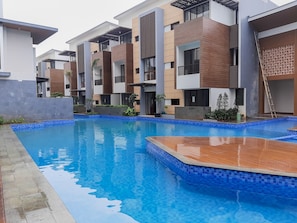 A modern residential building with a swimming pool, featuring a combination of brick and concrete facades, and a wooden deck area. - Homey and Simple 1BR at Asatti Apartment (Pagedangan)