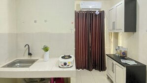 A kitchen with a sink, a toaster, a potted plant, a curtain, and a cabinet. - Strategic Studio Apartment at Casablanca East (Jakarta)
