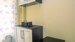 A small kitchenette with a black countertop, a water dispenser, and a cabinet above. - Strategic Studio Apartment at Casablanca East (Jakarta)