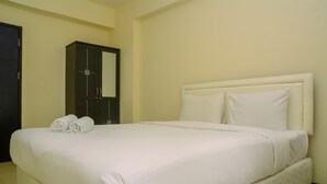A neatly made bed with white linens and pillows, a dark wooden wardrobe, and a plain wall. - Strategic Studio Apartment at Casablanca East (Jakarta)