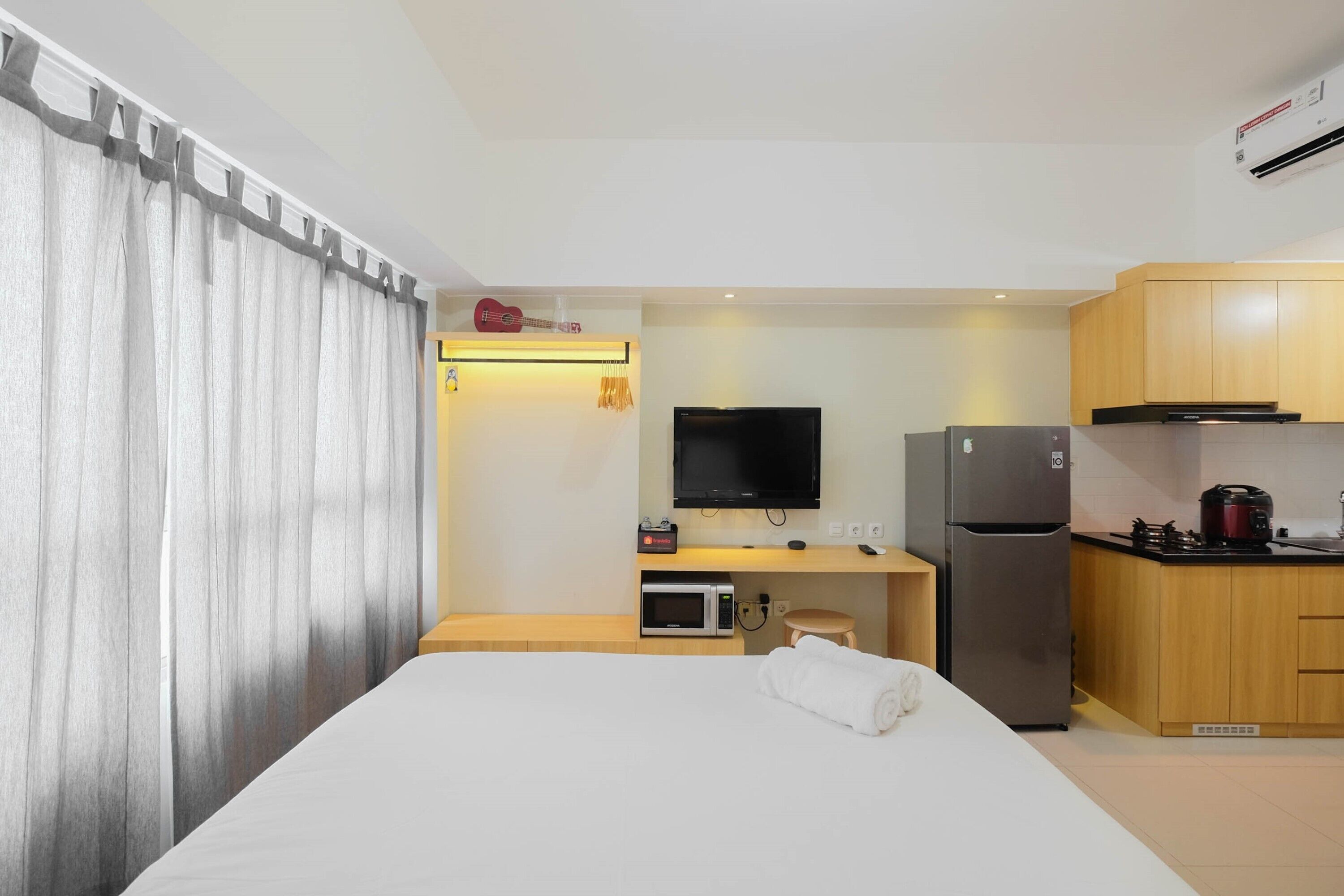 A hotel room with a bed, a TV, a microwave, a refrigerator, and a small kitchen area.