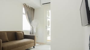 A living room with a beige sofa, a standing fan, and a TV mounted on the wall. - Comfy 2BR Apartment @ Springlake Summarecon (Bekasi)