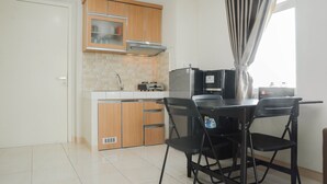 A compact kitchen with wooden cabinets, a built-in microwave, and a dining table with chairs. - Comfy 2BR Apartment @ Springlake Summarecon (Bekasi)