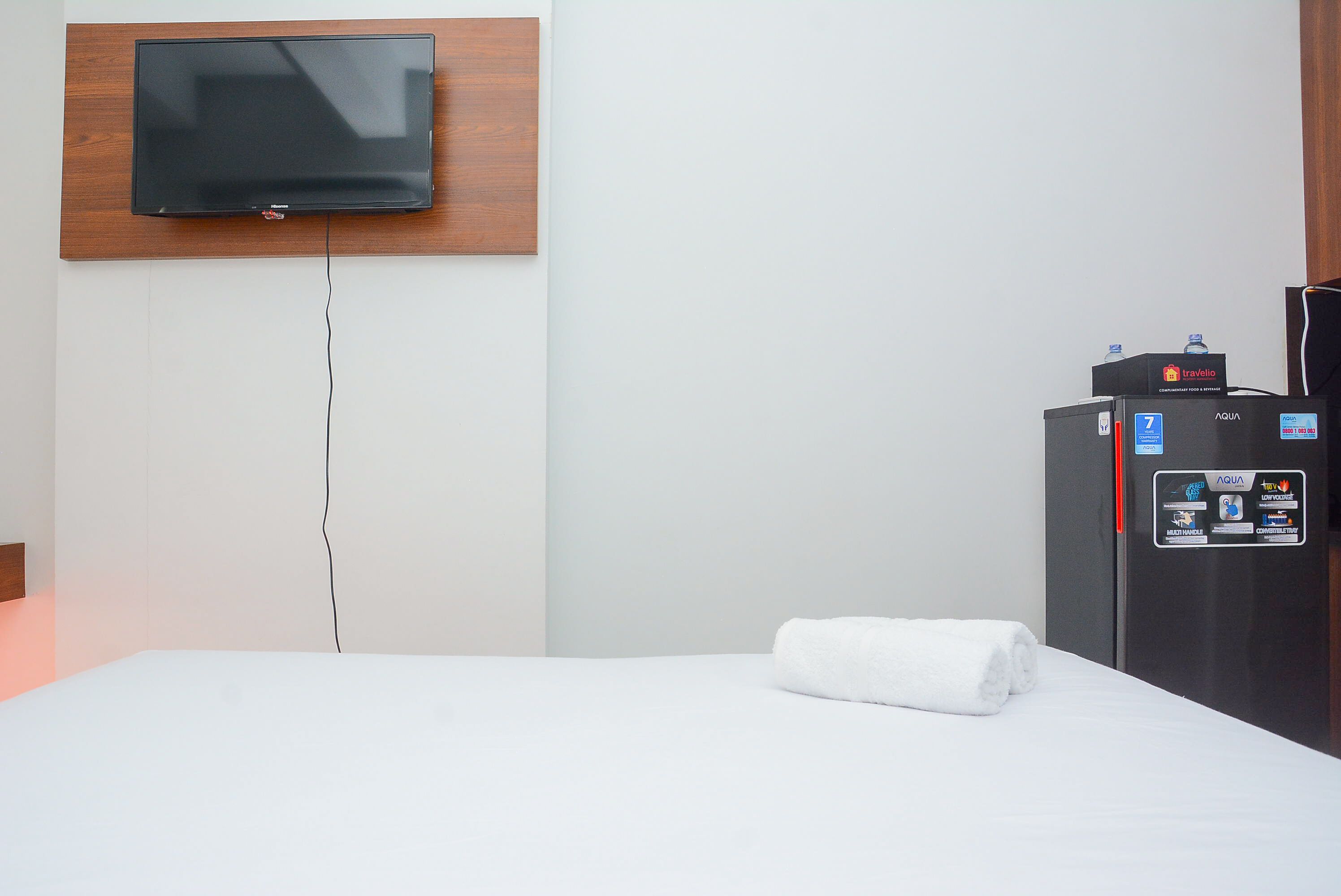 A hotel room with a bed, a television mounted on a wooden panel, and a minibar refrigerator.