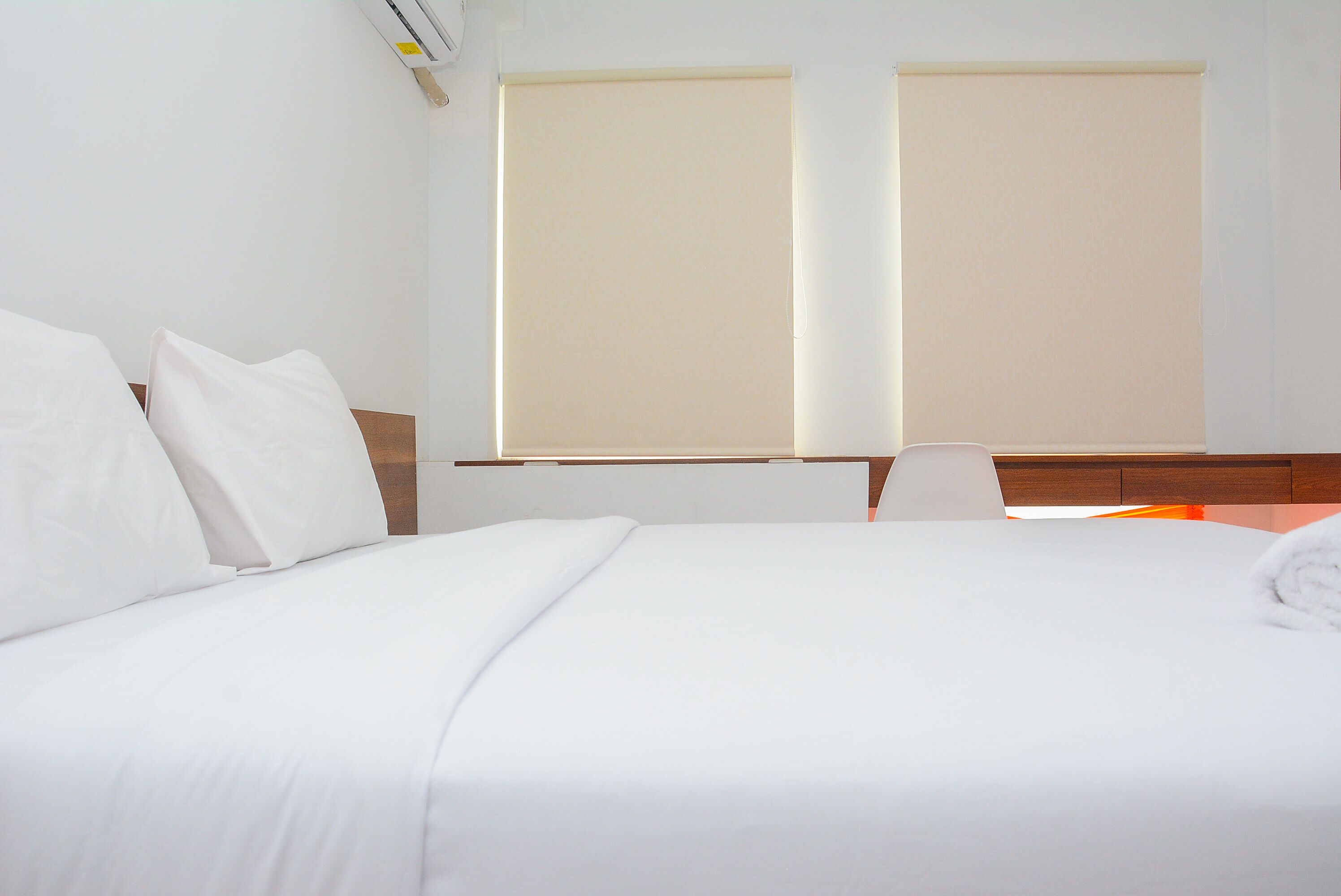 A hotel room with a bed, a desk, and two windows with blinds.
