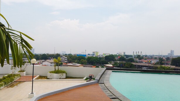A rooftop pool with a wooden deck and a view of the city skyline. - Comfy Studio Room at Patraland Urbano Apartment (Bekasi)