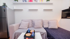 A modern living room with a sofa, a coffee table with a box of complimentary food and beverage, and a refrigerator. - Pool View and Homey 2BR Apartment @ Springlake Summarecon (Bekasi)