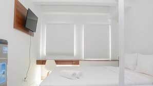 A hotel room with a bed, a TV mounted on the wall, a small table, and a window with blinds.
