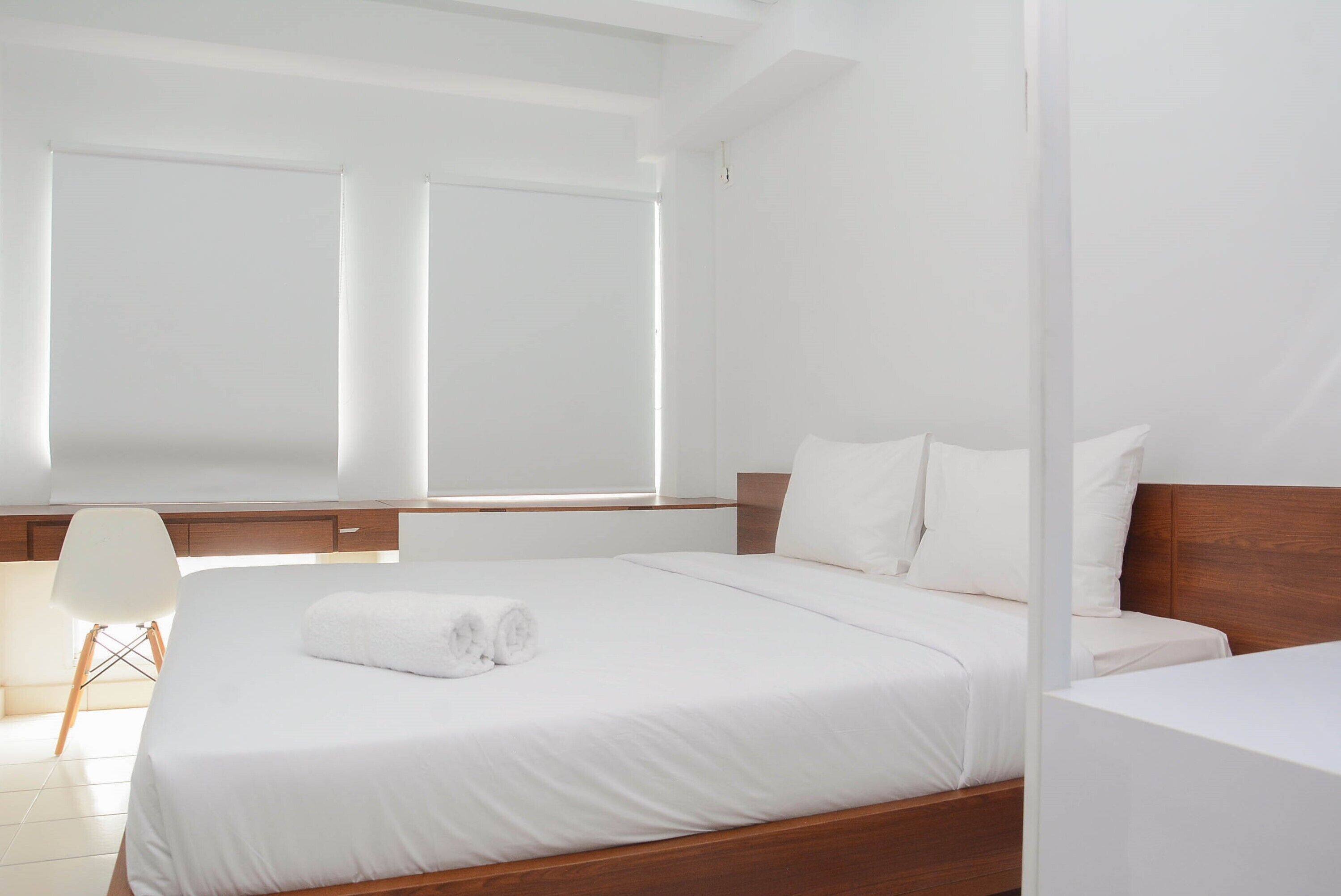 A modern hotel room with a large bed, white bedding, and a wooden headboard.