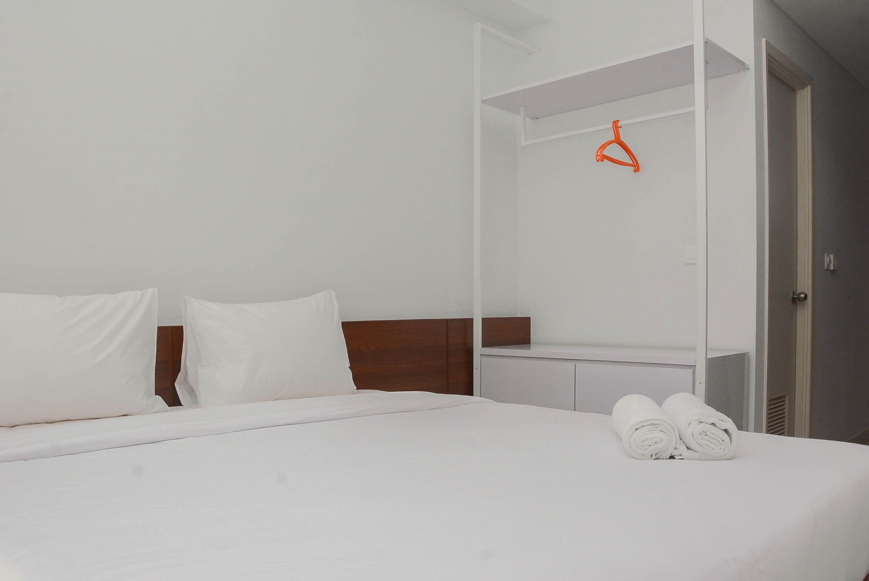 A neatly made bed with white linens, a wooden headboard, and a white nightstand with rolled towels.