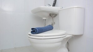 A white toilet with a blue towel on the lid, a white sink, and a toilet paper holder above the sink.