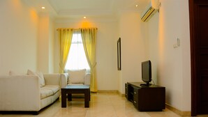 A living room with a sofa, a coffee table, a TV on a stand, and a window with curtains. - Modern 2BR at The Belleza Apartment (Jakarta)