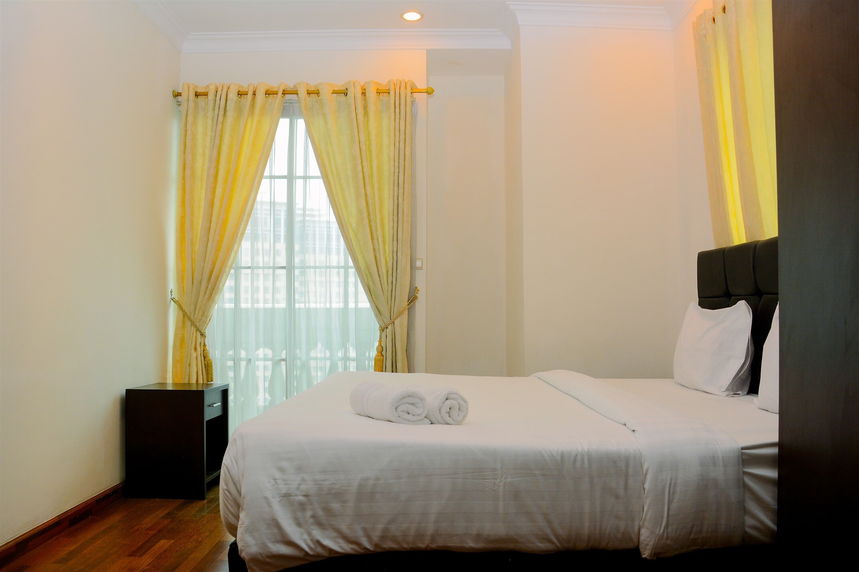 Una habitación de hotel con cama, cortinas, mesita de noche y ventana.