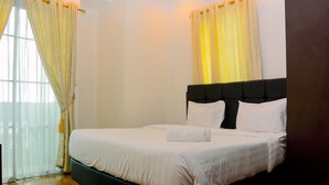 A neatly made bed with white linens and a folded towel, a dark headboard, and light-colored curtains. - Modern 2BR at The Belleza Apartment (Jakarta)