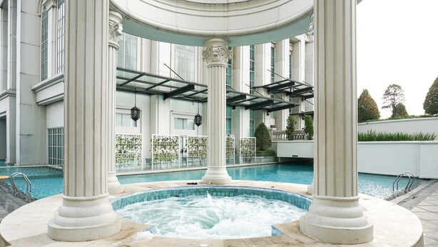 A hot tub surrounded by columns in an indoor setting with a pool in the background. - Modern 2BR at The Belleza Apartment (Jakarta)