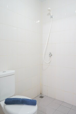 A bathroom with white tiles, a white toilet, and a shower with a hose.