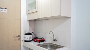 A small kitchen with a sink, a stove, and a cabinet. - Cozy Studio Apartment at Ayodhya Residences By Travelio (Tangerang)