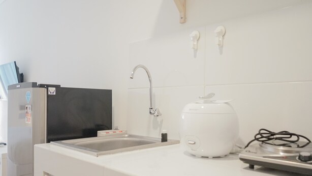 A kitchen with a refrigerator, a sink, and a coffee maker. - Cozy Studio Apartment at Ayodhya Residences By Travelio (Tangerang)