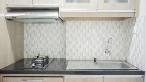 A kitchen with light wood cabinets, a stainless steel range hood, a black countertop, a sink with a faucet, and a tiled backsplash. - Comfy Studio at Trimezia Beverly Apartment By Travelio (Gading Serpong)