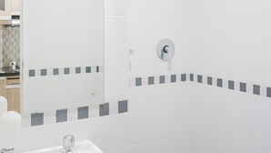A bathroom with a white sink, a shower with a handheld showerhead, and a tiled wall with a decorative border. - Comfy Studio at Trimezia Beverly Apartment By Travelio (Gading Serpong)
