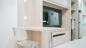 A modern kitchen with a built-in TV, white cabinetry, and a white chair. - Comfy Studio at Trimezia Beverly Apartment By Travelio (Gading Serpong)