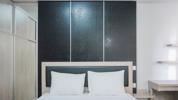 A modern bedroom with a large bed, a headboard with a decorative panel, and a bedside table. - Comfy Studio at Trimezia Beverly Apartment By Travelio (Gading Serpong)