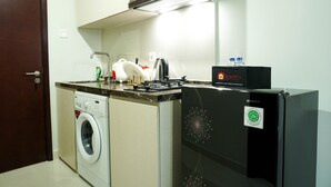 Une cuisine compacte équipée d’un lave-linge, d’un réfrigérateur noir et d’un plan de travail sur lequel se trouvent une machine à café et une boîte étiquetée « Voyageurs ».