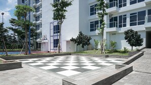 Une cour avec un sol à carreaux, entourée d’arbres et bordée d’un bâtiment moderne.