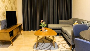 Una sala de estar con una mesa de centro de madera, un sofá, un televisor sobre un mueble de madera y una cortina al fondo.