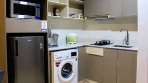 Una cocina compacta equipada con microondas, lavadora, hervidor y pileta.
