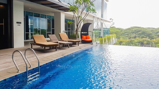 A modern hotel with a rooftop infinity pool, lounge chairs, and a view of lush greenery. - Chic Brooklyn Alam Sutera Studio Apartment By Travelio (South Tangerang)