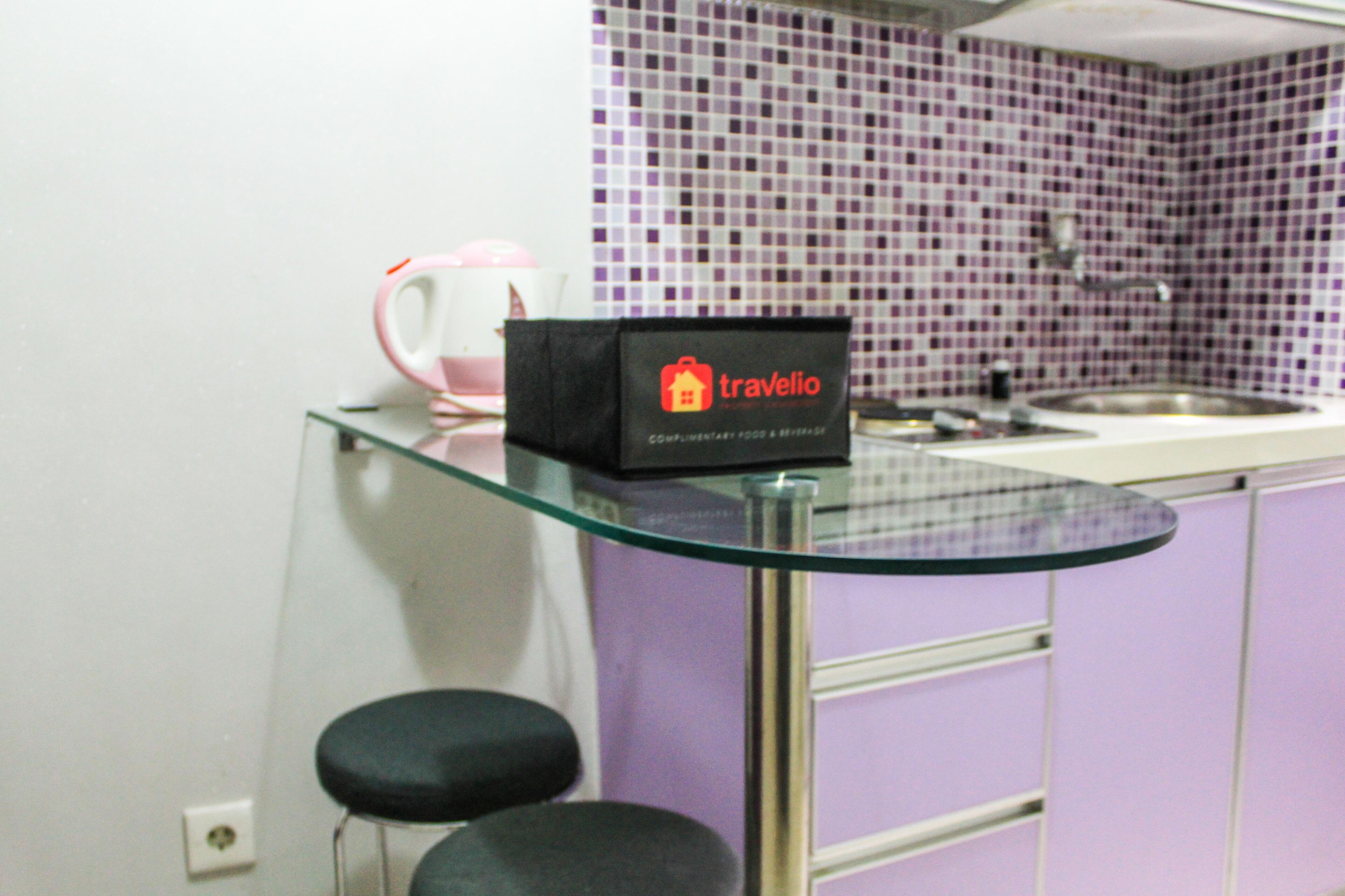 Una cocina con una mesa de vidrio, una bolsa de viaje y un hervidor rosa.