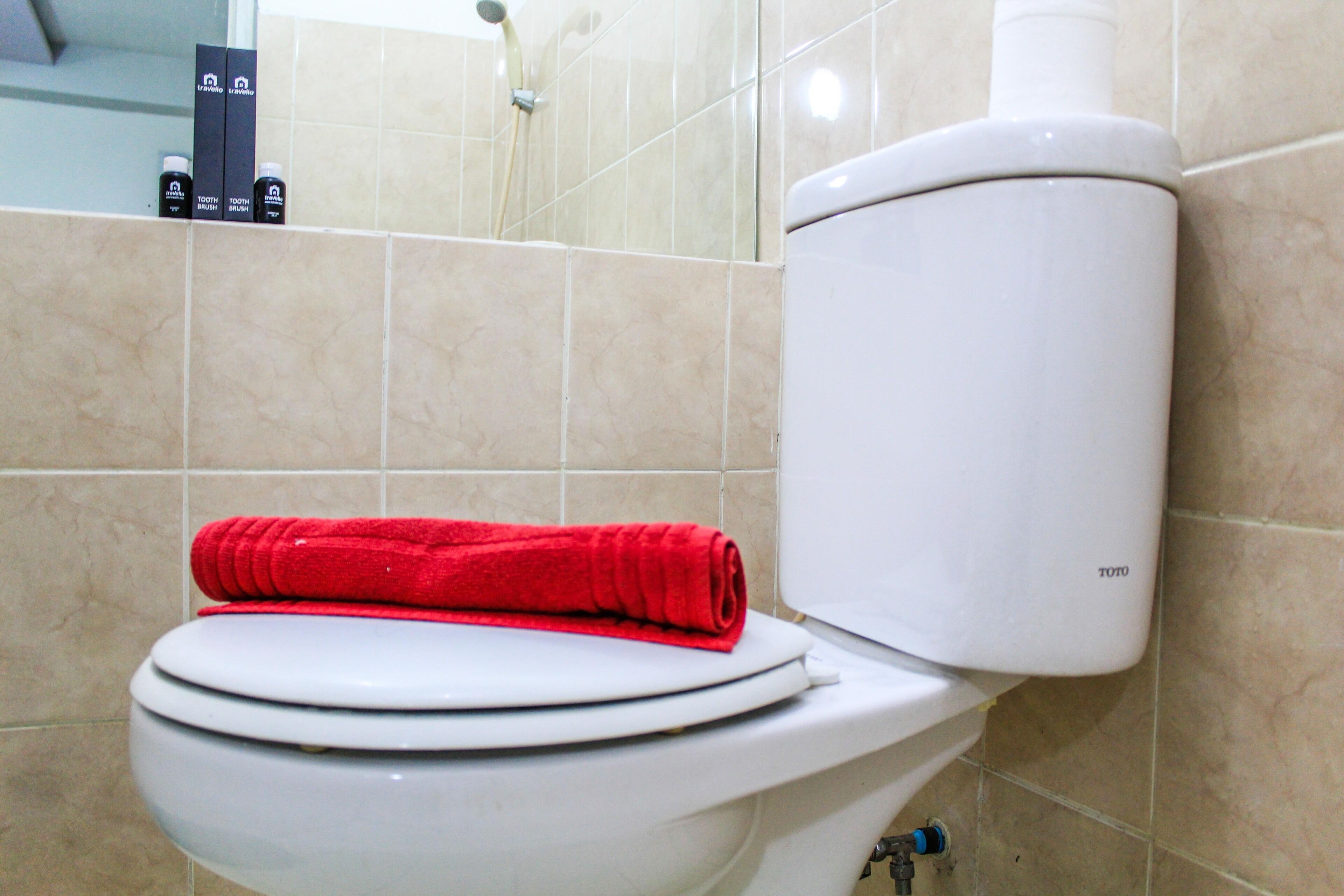 A toilet with a red towel on the seat and a TOTO brand toilet tank.