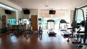 A gym with various exercise equipment, large windows, and a television. - Strategic Location 2BR Apartment at FX Residence By Travelio (Jakarta)