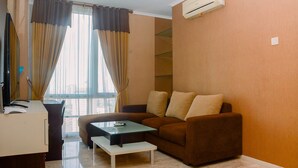 A living room with a brown sofa, a glass coffee table, and a TV on a wooden stand. - Strategic Location 2BR Apartment at FX Residence By Travelio (Jakarta)