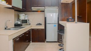 A compact kitchen with dark wooden cabinets, a white refrigerator, a microwave, and a gas stove. - Strategic Location 2BR Apartment at FX Residence By Travelio (Jakarta)
