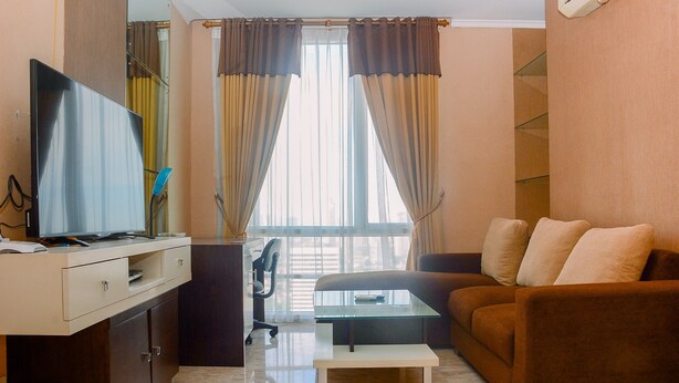 A living room with a sofa, a coffee table, a TV on a cabinet, and a window with curtains. - Strategic Location 2BR Apartment at FX Residence By Travelio (Jakarta)