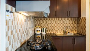 A kitchen with a gas stove, a sink, and a tiled backsplash. - Cozy 2BR at Empyreal Epicentrum Apartment By Travelio (Jakarta)