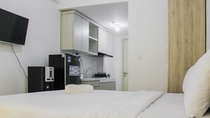 Ein Hotelzimmer mit Bett, Wandfernseher, einer Küchenzeile und einer Holztür.