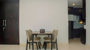 A dining area with a table and chairs, a small box on the table, and a dark door to the left. - Comfy and Spacious 2BR The Masterpiece Epicentrum Apartment By Travelio (Jakarta)