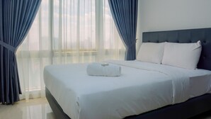 A neatly made bed with white linens and a rolled towel, a dark headboard, and sheer curtains allowing natural light. - Comfy and Spacious 2BR The Masterpiece Epicentrum Apartment By Travelio (Jakarta)