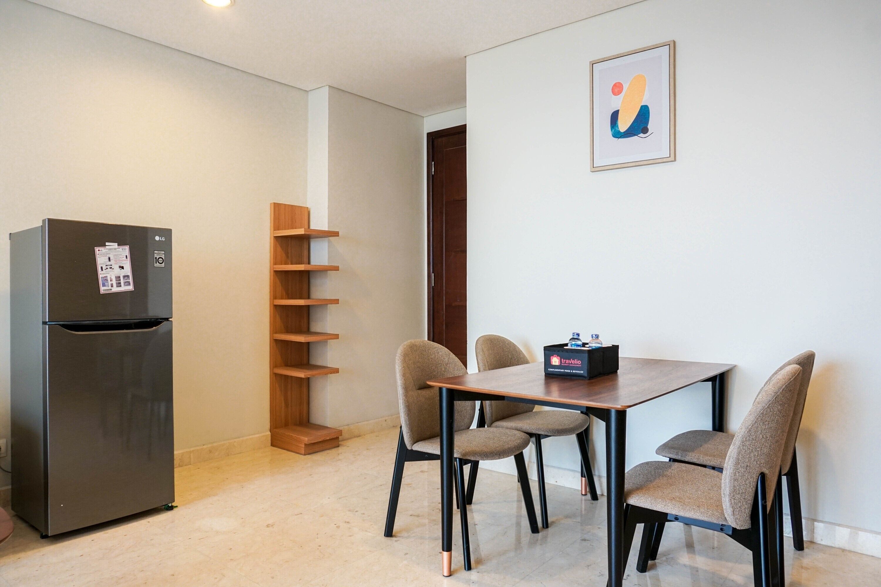 A compact living space with a kitchenette, a dining table with four chairs, a wooden shelf unit, and a framed abstract artwork on the wall.
