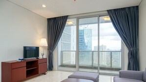 A modern living room with a flat-screen TV on a wooden cabinet, a sofa, and a large window with curtains. - Comfortable Deluxe 2BR at The Empyreal Condominium Epicentrum Apartment By Travelio (Jakarta)
