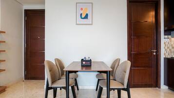 A dining area with a wooden table and four chairs, a framed artwork on the wall, and two wooden doors.