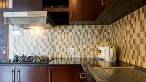 A kitchen with wooden cabinets, a stainless steel sink, a gas stove, and a coffee maker. - Comfortable Deluxe 2BR at The Empyreal Condominium Epicentrum Apartment By Travelio (Jakarta)