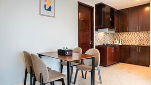 A compact kitchen with dark wood cabinets, a tiled backsplash, and a small dining area with two chairs and a table. - Comfortable Deluxe 2BR at The Empyreal Condominium Epicentrum Apartment By Travelio (Jakarta)
