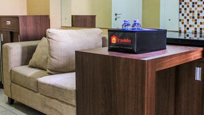 A compact living space with a sofa, a wooden side table, and a box labeled 'Travelio' on the table. - Comfortable and Tranquil 2BR Apartment at Green Pramuka By Travelio (Jakarta)