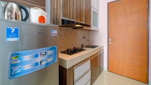 Cocina compacta con refrigerador, tetera, estufa y lavamanos. Puerta de madera y salpicadero de azulejos.